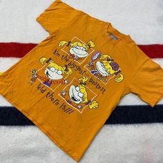 a yellow t - shirt with cartoon characters on it sitting on a white and blue striped surface