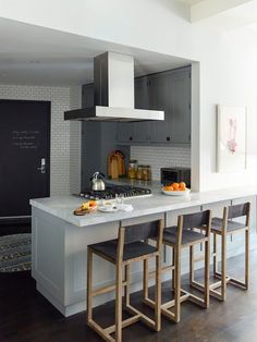 a kitchen with white counter tops and wooden stools in front of an island topped with fruit