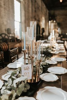 a long table is set with white plates and silverware, greenery and candles