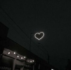 a neon heart is hanging in the air above a dark city street at night time