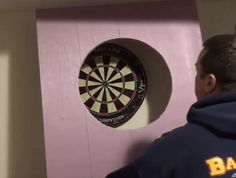 a man standing next to a pink wall with a dart in it's center