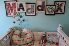 a baby's crib with pillows and letters on the wall