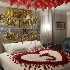 a bed with red rose petals and balloons in the shape of a heart