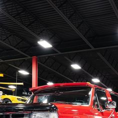 an old red truck is parked in a garage with other classic cars and trucks behind it