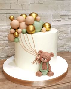 a white cake with gold balloons and a teddy bear