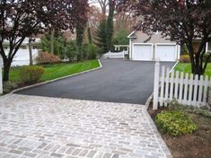 a driveway with a white picket fence and trees