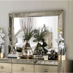 a mirror sitting on top of a dresser with vases and flowers in front of it