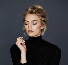 a woman with blonde hair wearing a black turtle neck sweater and holding her hand to her chin