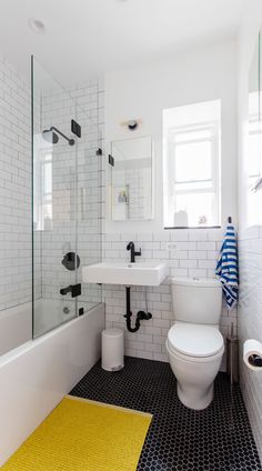 a white toilet sitting next to a bath tub in a bathroom under a window on top of a tiled floor