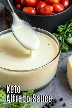 a spoon full of keto alfredo sauce with tomatoes in the background and text overlay that reads, keto alfredo sauce