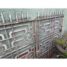 an old iron gate with decorative designs on the side of a building next to a potted plant