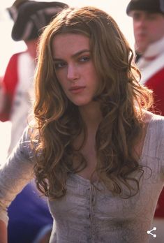 a woman with long brown hair standing in front of other people and looking at the camera