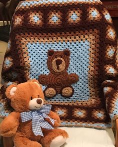 a brown teddy bear sitting on top of a chair next to a crocheted blanket