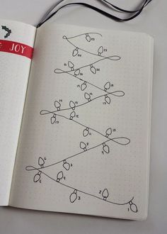 an open notebook with a christmas tree drawn on the page and red ribbon hanging from it