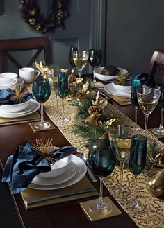 the table is set for christmas dinner with blue and gold decorations on it, along with wine glasses