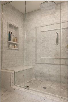 a walk in shower sitting next to a white tiled wall with shelves on the side