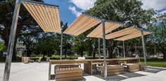 an outdoor seating area with wooden benches and pergolated roof overhangs in a park