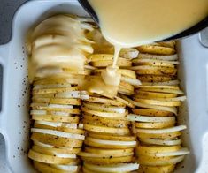 a container filled with sliced potatoes covered in cheese and dressing being drizzled on top