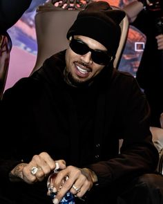 a man in black jacket and sunglasses sitting on a chair with other people behind him