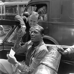 black and white photograph of two men sitting in the back of a car, one holding a cell phone