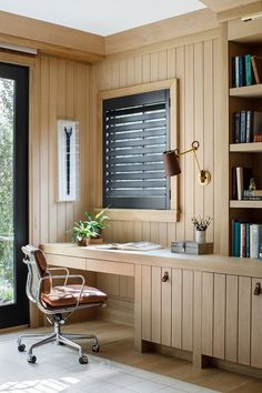 a desk with a chair and bookshelf in front of a window that has shutters on it