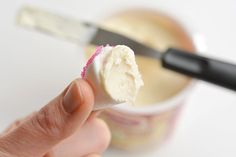 a hand holding a piece of cake in front of a cup with icing on it