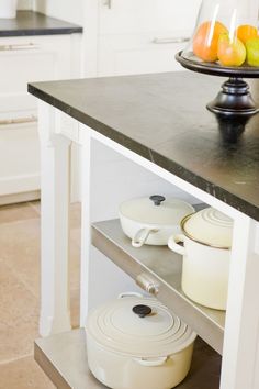 a kitchen island with pots and pans sitting on it's shelf next to fruit