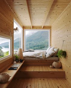 a bedroom with wooden walls and flooring has a large window that looks out onto the mountains