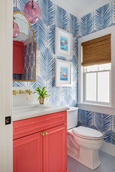 a bathroom with blue and white wallpaper, pink cabinetry, and a toilet