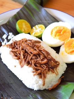 a plate with rice, hard boiled eggs and meat on it next to sliced oranges