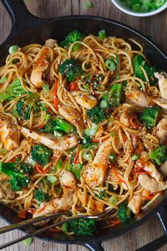 a skillet filled with chicken, broccoli and noodles on top of a wooden table