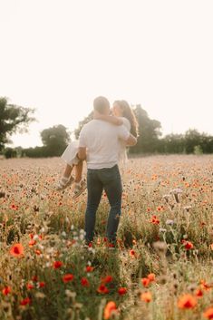 a man and woman standing in a field full of flowers with their arms around each other