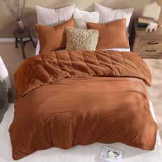 a bed with brown sheets and pillows on top of it in a bedroom next to a white rug