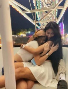 two women hugging each other while sitting on a boat in the water at night time