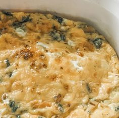 a casserole dish with cheese and spinach on top in a white pan