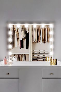 an illuminated vanity mirror in front of a white dresser with drawers and clothes on it