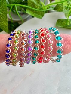 four different colored bracelets sitting on top of a person's hand with green leaves in the background