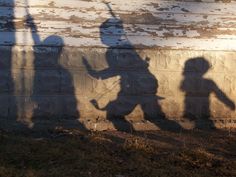 the shadow of two children playing with a frisbee in front of a brick wall