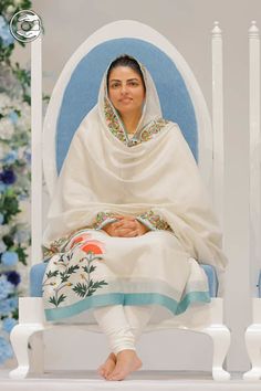 a woman sitting in a chair with a blanket over her head and flowers on the wall behind her