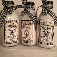 three glass bottles with labels on them sitting on a shelf next to another bottle that has a black and white ribbon tied around it