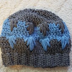 a crocheted hat with blue and gray leaves on the side sitting on a white carpet