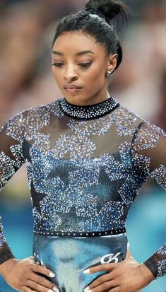 a woman with her hands on her hips wearing a blue and black dress while standing in front of a crowd