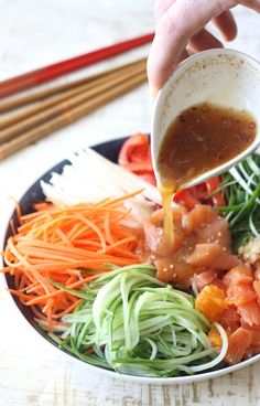 someone pouring sauce on a plate of food with carrots and other veggies