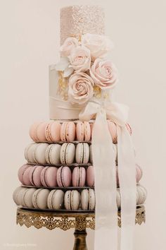 a wedding cake with macaroons and roses on top is displayed in front of a stack of macaroons