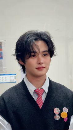 a young man wearing a vest and tie with buttons on his lapel, looking at the camera