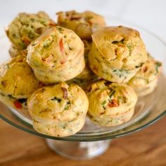 a glass plate filled with muffins on top of a wooden table