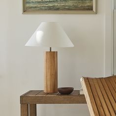 a wooden table with a lamp on it next to a painting and a chair in the background