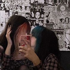 two girls with dyed hair are looking at their cell phones in front of a wall full of comic books