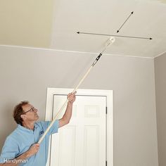 a man is painting the ceiling in his living room with white paint and a mop