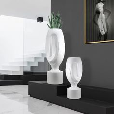 two white vases sitting next to each other on top of black stands in a room